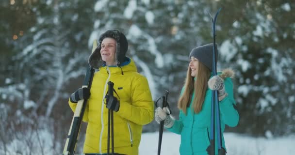 Retrato de larga duración de una joven pareja activa disfrutando esquiando en el bosque invernal nevado, enfoque en la mujer sonriente en frente, espacio para copiar — Vídeo de stock