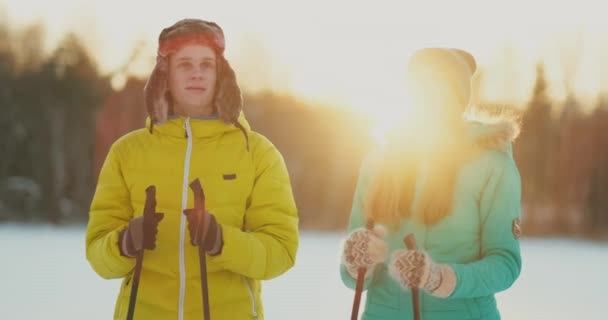 Dans la forêt d'hiver au coucher du soleil un homme et une femme skient et regardent autour de la beauté de la nature et des attractions au ralenti . — Video
