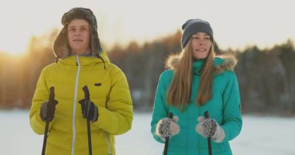 In the winter forest at sunset loving couple skiing and look around at the beauty of nature and attractions in slow motion. — Stock Video