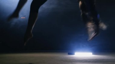 Yetenekli kız jimnastikçi close-up bir takla duman konturlu bir ışık ağır çekimde jimnastik halı üzerinde gerçekleştirir. Steadycam