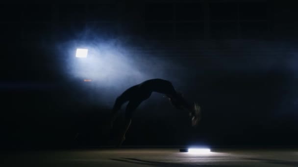 Chica talentosa gimnasta realiza volteretas en la alfombra de gimnasia en cámara lenta en la luz en el humo . — Vídeos de Stock