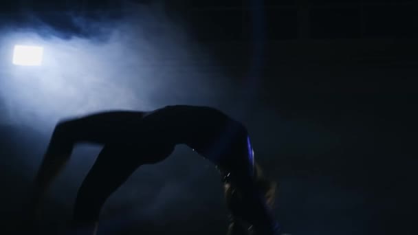 Detail o talentované gymnastka dívka provádí kotrmelec na gymnastický koberec v pomalém pohybu v tvarovaná světla v kouři. — Stock video