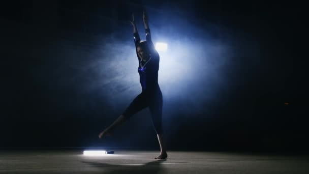 A girl performs a jump gymnastics on a dark background in the smoke — Stock Video