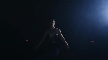 Genç kadın jimnastikçi kameraya ararken çalışır ve ileri flip ve vidalı hava duman halıda spor salonunda ağır çekimde gerçekleştirir. Steadicam hareket