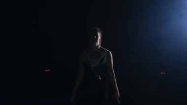 Genç kadın jimnastikçi kameraya ararken çalışır ve ileri flip ve vidalı hava duman halıda spor salonunda ağır çekimde gerçekleştirir. Steadicam hareket ve arka ışık