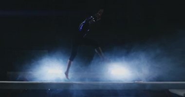 Profesyonel jimnastikçi kız denge aleti yavaş çekimde bir atlayış bir spin ile gerçekleştirir. Spor salonunda duman mavi renk. Jimnastik yarışmaları.