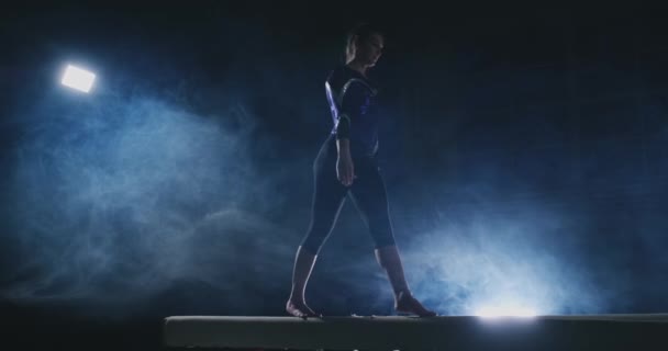 Chica gimnasta profesional realiza un salto con un giro en la viga de equilibrio en cámara lenta. Color azul humo en el gimnasio — Vídeos de Stock