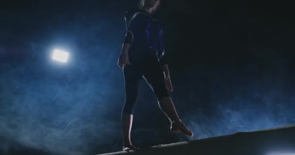 Gros plan du pied d'une fille gymnaste professionnel effectue un saut avec rotation sur le faisceau d'équilibre au ralenti. Couleur bleu fumée dans la salle de gym. Concours de gymnastique — Video