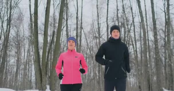 Un hombre y una mujer con una chaqueta rosa en el invierno corriendo por el parque en cámara lenta. Estilo de vida saludable — Vídeos de Stock