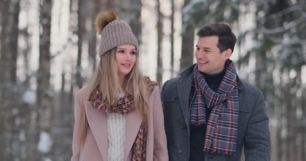 Nella foresta innevata invernale, giovani uomini e donne vestiti con cappotti e sciarpe camminano e si divertono. Amare coppia trascorrere insieme San Valentino giorno . — Video Stock