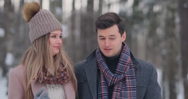 Un hombre joven y una mujer en un abrigo se divierten y juegan con la nieve en un bosque de invierno en cámara lenta. Felicidad y sonrisas en las caras — Vídeos de Stock