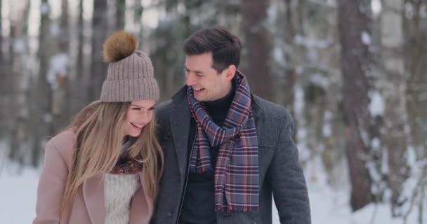 Молодая супружеская пара гуляет по зимнему лесу. Мужчина и женщина смотрят друг на друга смеясь и улыбаясь в замедленной съемке . — стоковое видео