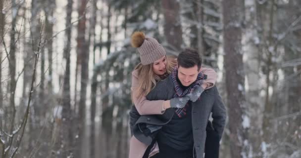 Un jeune homme et une femme en manteau s'amusent et jouent avec la neige dans une forêt d'hiver au ralenti. Bonheur et sourires sur les visages — Video