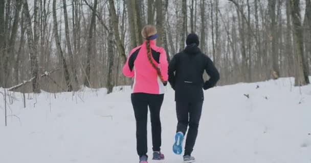 Θετικά όμορφα υγιή ζευγάρι τρέξιμο με αθλητικά είδη μέσα από το δάσος το πρωί ηλιόλουστο χειμώνα. η θέα από πίσω — Αρχείο Βίντεο