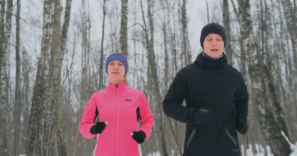 Positiv vackra unga friska par körs med sportkläder genom skogen i den soliga vintermorgon. — Stockvideo