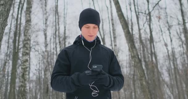 フィットネス スポーツ 健康的なライフ スタイル コンセプト 音楽を聴くと冬道 イメージに沿って実行しているスマート フォンをイヤホンで幸せな若い男 — ストック動画