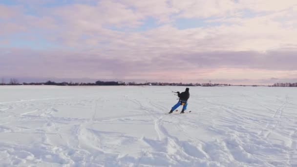 Ein Mann fährt bei Sonnenuntergang im Schnee auf einem Feld Ski. Sein Fallschirm zieht. Kitesurfen im Schnee.. — Stockvideo