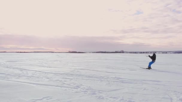 Carrera de competición de kite de nieve de invierno extremo aéreo 4K con diferentes cometas de nieve de colores, esquí, snowboarders sobre el lago de hielo en frente de la ciudad en la ventisca y el clima de nieve del dron — Vídeo de stock