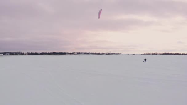 スローモーション: オスの運動選手はスキーでカイトに取り組んでいます。彼は大きな湖の氷の上にロールバックします。ローリングは、彼はさまざまなジャンプ、クーデターや他の演習を実行します。風の強い晴れた冬の日 — ストック動画