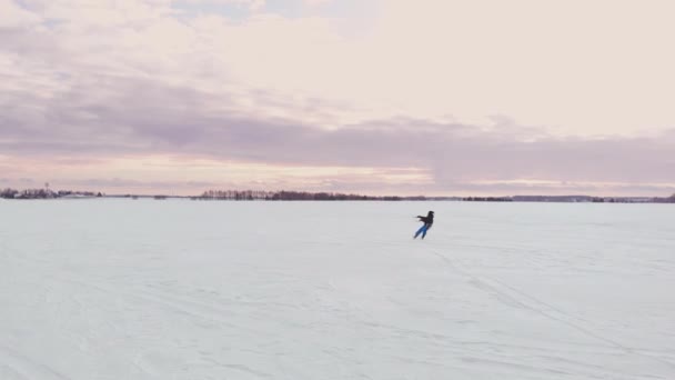 Een man is skiën in de sneeuw in een veld bij zonsondergang. Zijn parachute trekt. Kite surfen in de sneeuw.. — Stockvideo