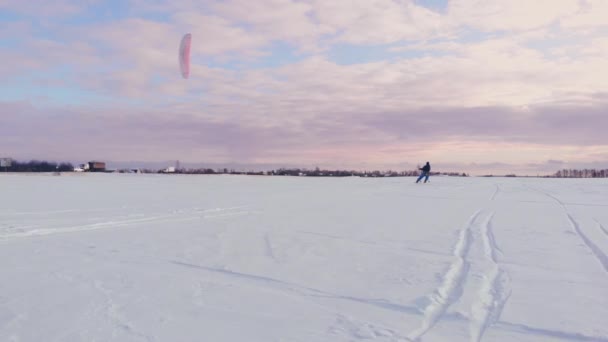 スポーツの服装の男性アスリートがカイトの美しい冬の風景に雪をやっています。. — ストック動画