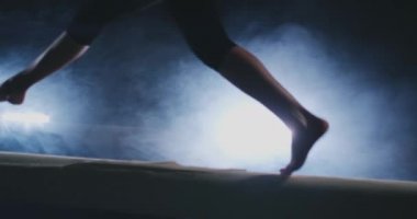Bir profesyonel jimnastikçi kız duman yavaş çekimde bir denge denge aletinin üstüne atlama ayak close-up. Bayan jimnastik. Grace ve sağlıklı bir yaşam tarzı