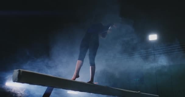 Piernas Chica profesional gimnastas saltar en cámara lenta en el humo en la viga de equilibrio. Gimnasia artística para mujer — Vídeos de Stock