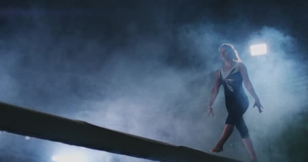 Het meisje is dat een professioneel atleet presteert gymnastische acrobatische truc op een balk in tegenlicht en slow in sport gymnastiek kleding. Rook en blauw. Springen en draaien op de evenwichtsbalk — Stockvideo