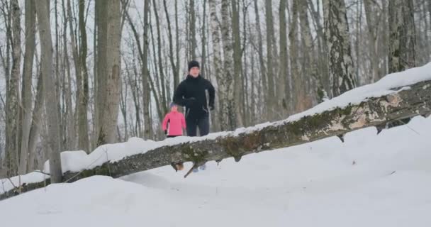 Un hombre y una mujer corren en el parque en invierno y saltan sobre un árbol caído. Paso sobre el obstáculo — Vídeos de Stock