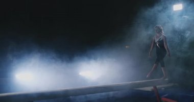 Kız bir numara bir günlüğüne arka ışık ve jimnastik spor giyim ağır çekimde gerçekleştirir. Duman ve mavi. Atlama ve denge aleti spin