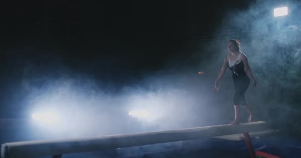 Dziewczyna wykonuje trick na dziennik w podświetlenie i zwolnionym tempie w sportowe gimnastyczne odzież. Dym i niebieski. Skok i spin na belki wagi — Wideo stockowe