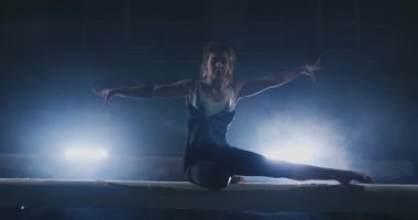 Profesyonel bir atlet bir ışının içinde arka ışık ve jimnastik spor giyim ağır çekimde jimnastik akrobatik numara gerçekleştirir kızdır. Duman ve mavi. Atlama ve denge aleti spin
