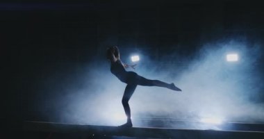 Profesyonel bir atlet bir ışının içinde arka ışık ve jimnastik spor giyim ağır çekimde jimnastik akrobatik numara gerçekleştirir kızdır. Duman ve mavi. Atlama ve denge aleti spin
