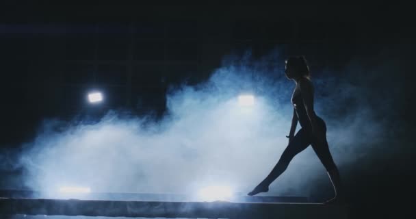 Sidovy av en kvinnlig gymnast gör split handstand på skoparmen mot svart bakgrund. — Stockvideo