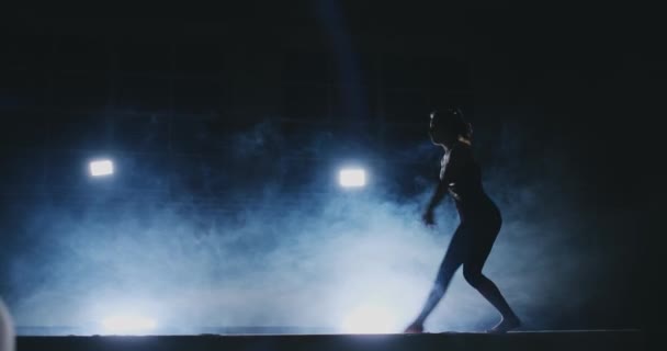 Gymnastique artistique féminine. Au ralenti dans la fumée, la jeune fille exécute des éléments complexes du programme olympique sur un faisceau d'équilibre . — Video