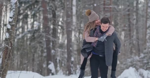 Pareja feliz está jugando juego de invierno afuera disfrutando de la luz del sol y el clima cálido de invierno en las montañas. fuerte chico es llevar novia en su hombros y giros su — Vídeos de Stock