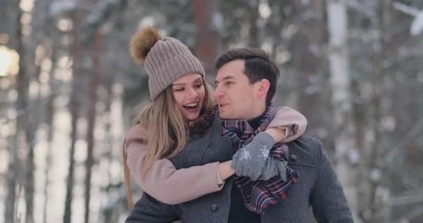 Pareja feliz está jugando juego de invierno afuera disfrutando de la luz del sol y el clima cálido de invierno en las montañas. fuerte chico es llevar novia en su hombro y giros ella en azul cielo fondo — Vídeo de stock