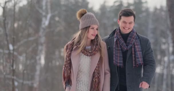 Młode małżeństwo w miłości spaceru w lesie zimą. Mężczyzna i kobieta spojrzeć na siebie, śmiech i uśmiech w zwolnionym tempie. Historia miłości Walentynki. — Wideo stockowe