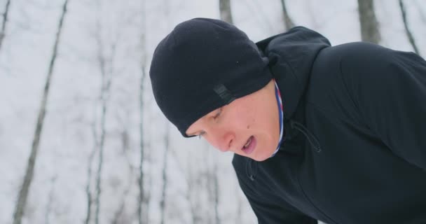一个年轻人在冬天的森林里晨跑累了, 停下来喘口气。他恢复了体力, 克服了疲劳, 继续跑。毅力和克服弱点 — 图库视频影像