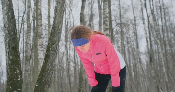 Молода жінка на ранковому бігу в зимовому лісі втомилася і перестала вдихати. Він відновив свою силу і подолав втому і продовжував бігати. Постійність і подолання слабкості — стокове відео