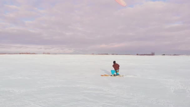 Een man is skiën in de sneeuw in een veld bij zonsondergang. Zijn parachute trekt. Kite surfen in de sneeuw.. — Stockvideo