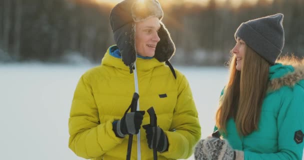 Een man in een gele jas en een meisje in een blauwe jumpsuit skiën in slow motion bij zonsondergang — Stockvideo