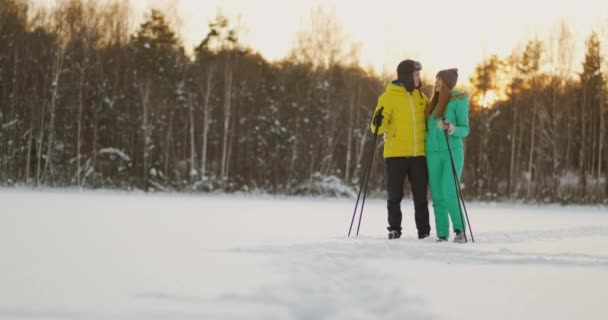 En el bosque de invierno al atardecer, un hombre y una mujer esquian y miran a su alrededor la belleza de la naturaleza y las atracciones en cámara lenta. . — Vídeo de stock