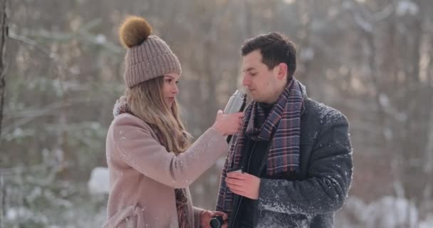 Ein fürsorglicher Mann wärmt seine Frau im Winter auf der Straße in einem verschneiten Park — Stockvideo