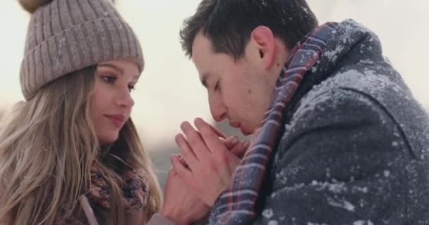 Um homem carinhoso aquece as mãos de suas esposas no inverno na rua em um parque coberto de neve . — Vídeo de Stock