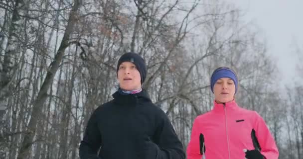 Positive beautiful young healthy couple running with sportswear through the forest in the winter morning — Stock Video