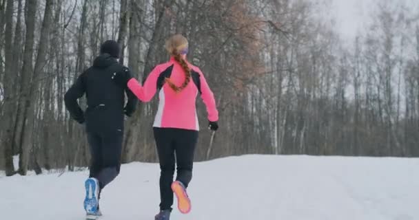 Mladé rodiny pár muž a žena na ráno běhat v zimním lese. Žena v uvolněné bunda muž v černém kabátku je běh přes zimní park. Šťastná rodina zdravého životního stylu — Stock video