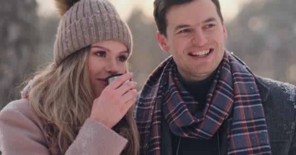 Couple heureux tenant des tasses de thé chaud sur le paysage hivernal. Jeune couple amoureux en vacances d'hiver, debout à côté d'un arbre et boire une tasse de thé chaud — Video