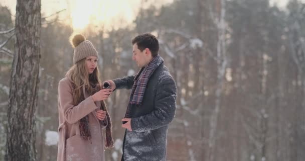 Pár v lásce v zimním lese pít čaj z termosky. Stylový muž a žena v plášti v parku v zimě na procházku. — Stock video