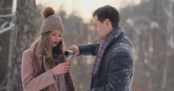 Casal feliz segurando xícaras de chá quente durante a paisagem de inverno. Jovem casal apaixonado em umas férias de inverno, de pé ao lado de uma árvore e beber uma xícara de chá quente — Vídeo de Stock